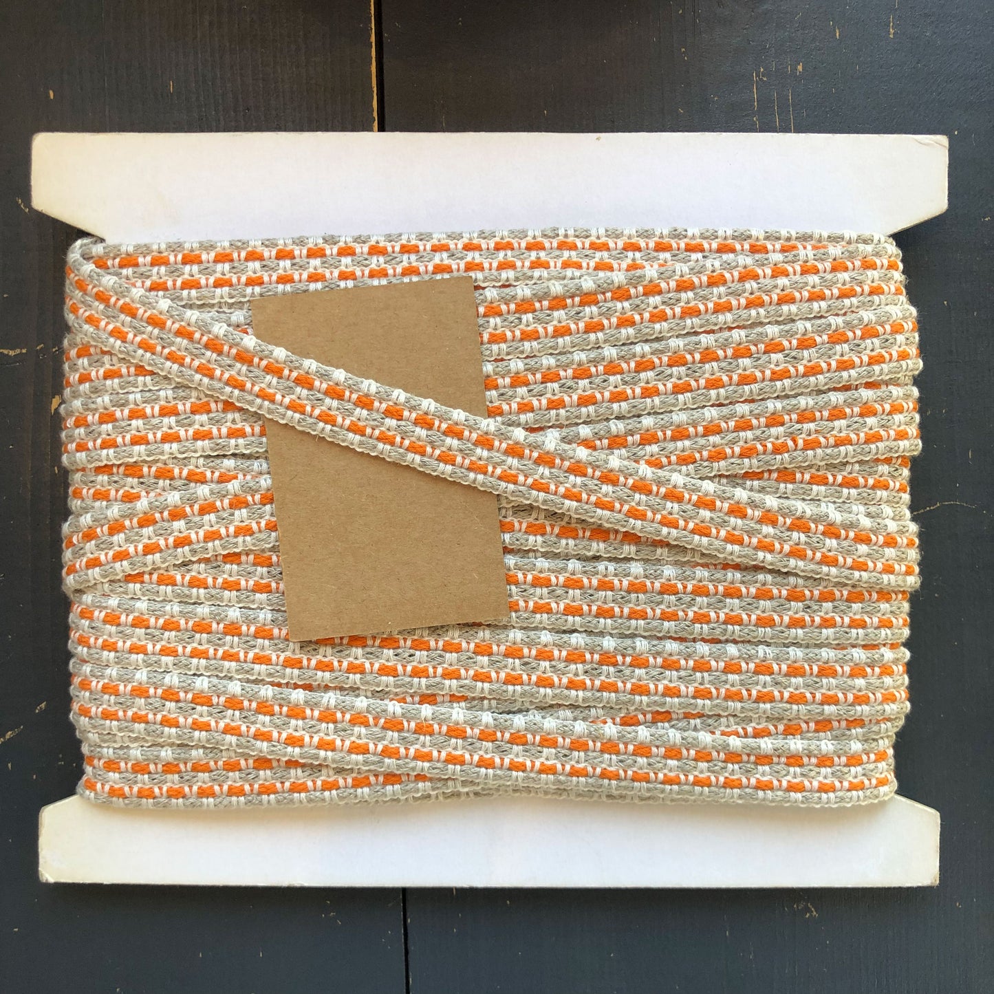 Een robuuster sierband met een geweven structuur van naturel beige en levendig oranje. Deze band heeft een ambachtelijke, stoere uitstraling en is ideaal voor het afwerken van kussens, tassen, wandhangers, andere interieurprojecten of kleding.