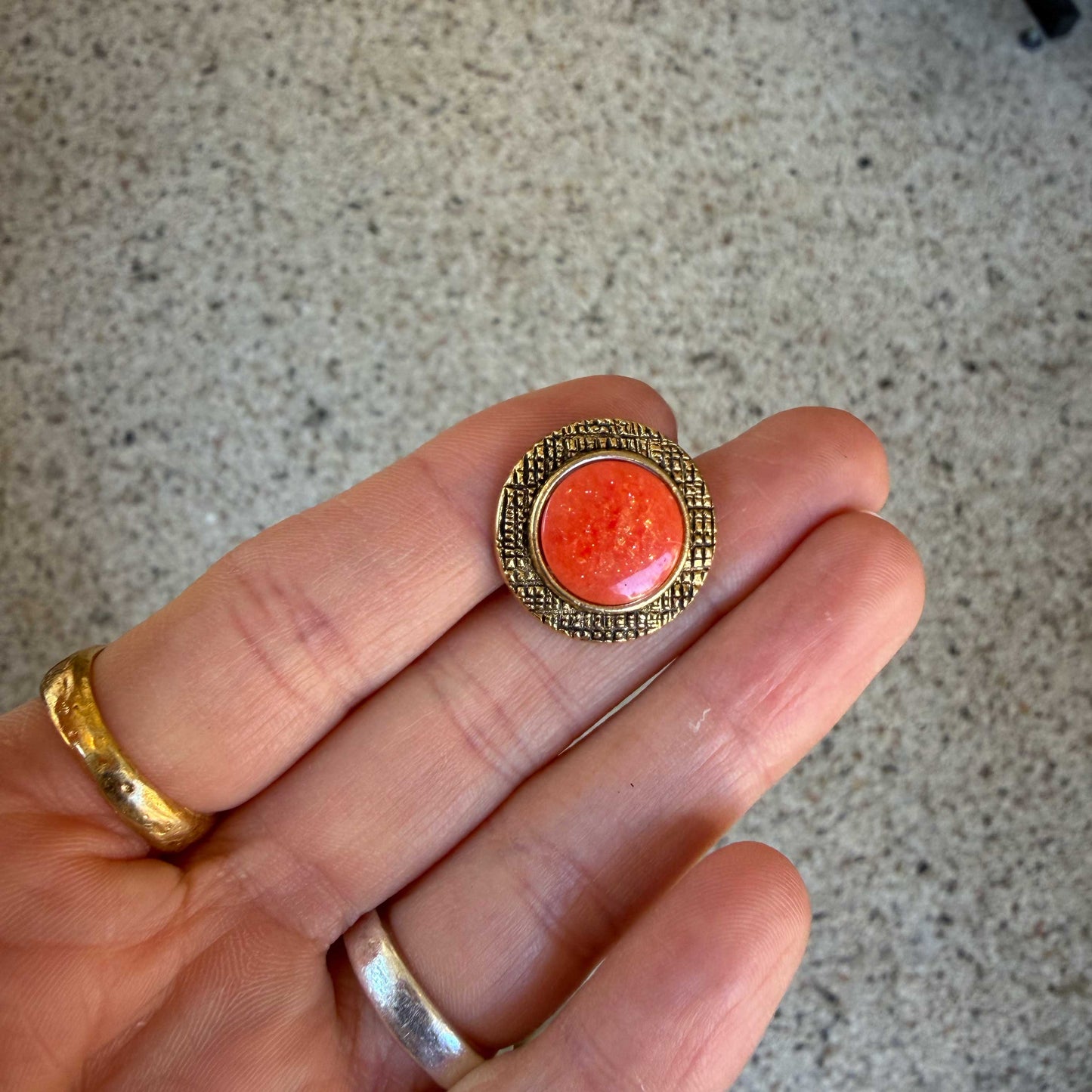 Deze bijzondere knoop combineert een warme goudkleurige rand met een sprankelende zalmroze kern.