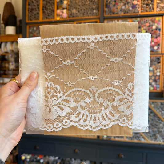 Dit verfijnde witte kant van 15 cm breed heeft een elegante en luchtige uitstraling. Het delicate patroon en de lichte transparantie geven elk ontwerp een zachte, romantische touch.