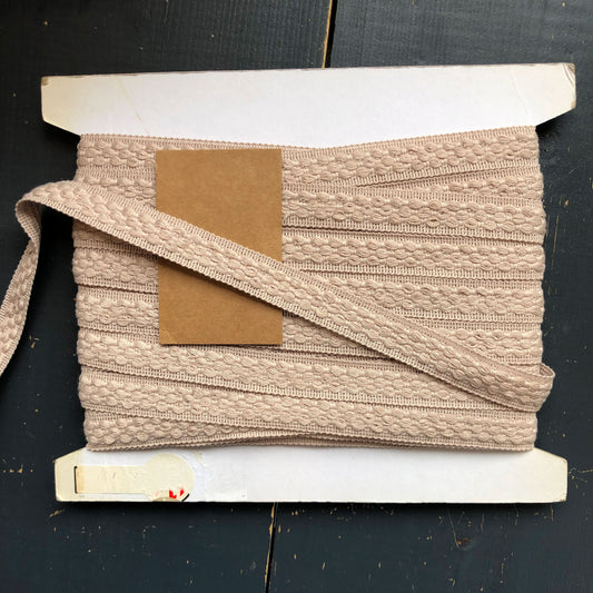 Een neutrale maar verfijnde sierband in een zachte beige tint. De band is voorzien van een elegant geweven structuur die zorgt voor een subtiel reliëfeffect. 