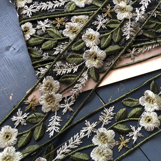 Dit prachtige sierband in een groen tinten heeft geborduurde bloemen en bladeren op een zwarte mesh achtergrond.