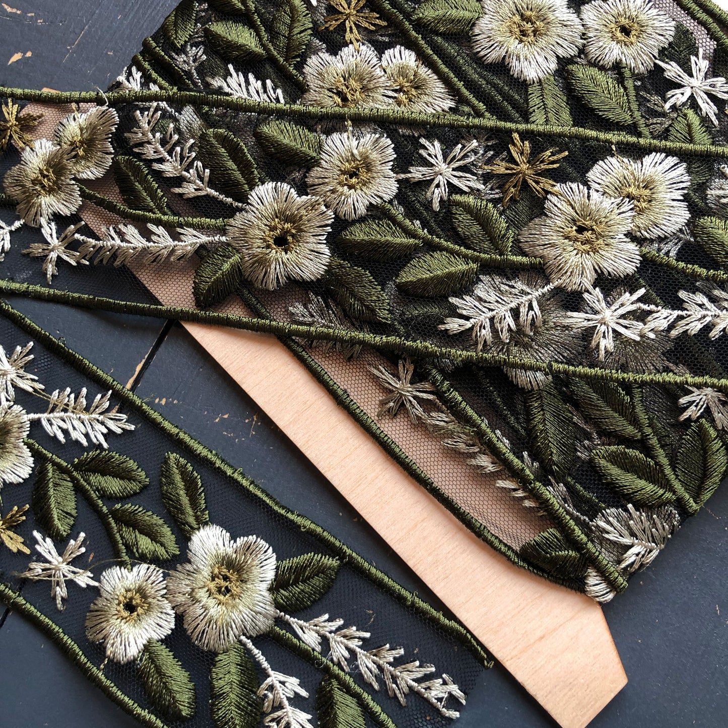 Dit prachtige sierband in een groen tinten heeft geborduurde bloemen en bladeren op een zwarte mesh achtergrond.