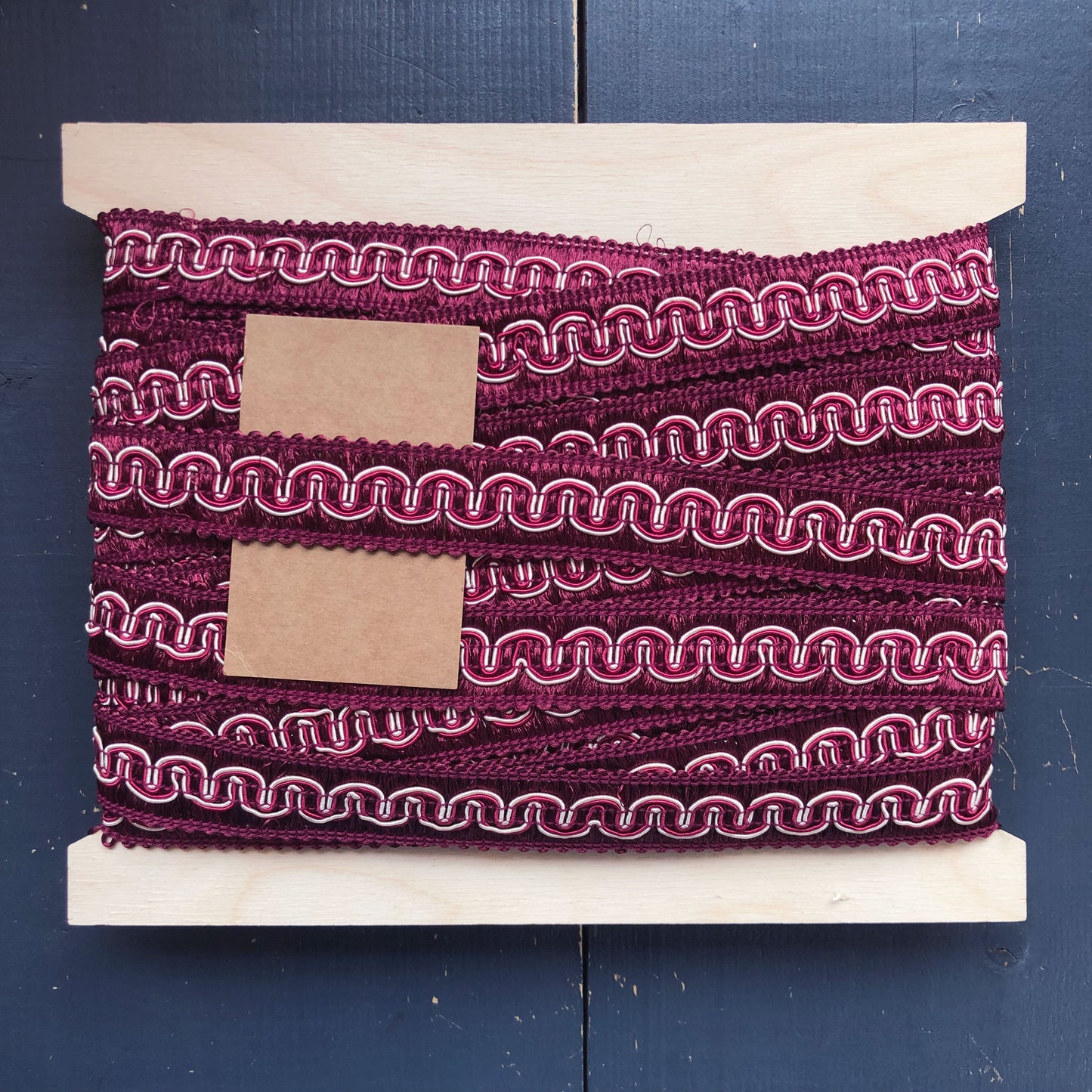 Een luxe sierband met een rijke wijnrode kleur en decoratieve ingeweven golvende lijnen in wit en roze. Deze band heeft een klassieke, bijna barokke uitstraling