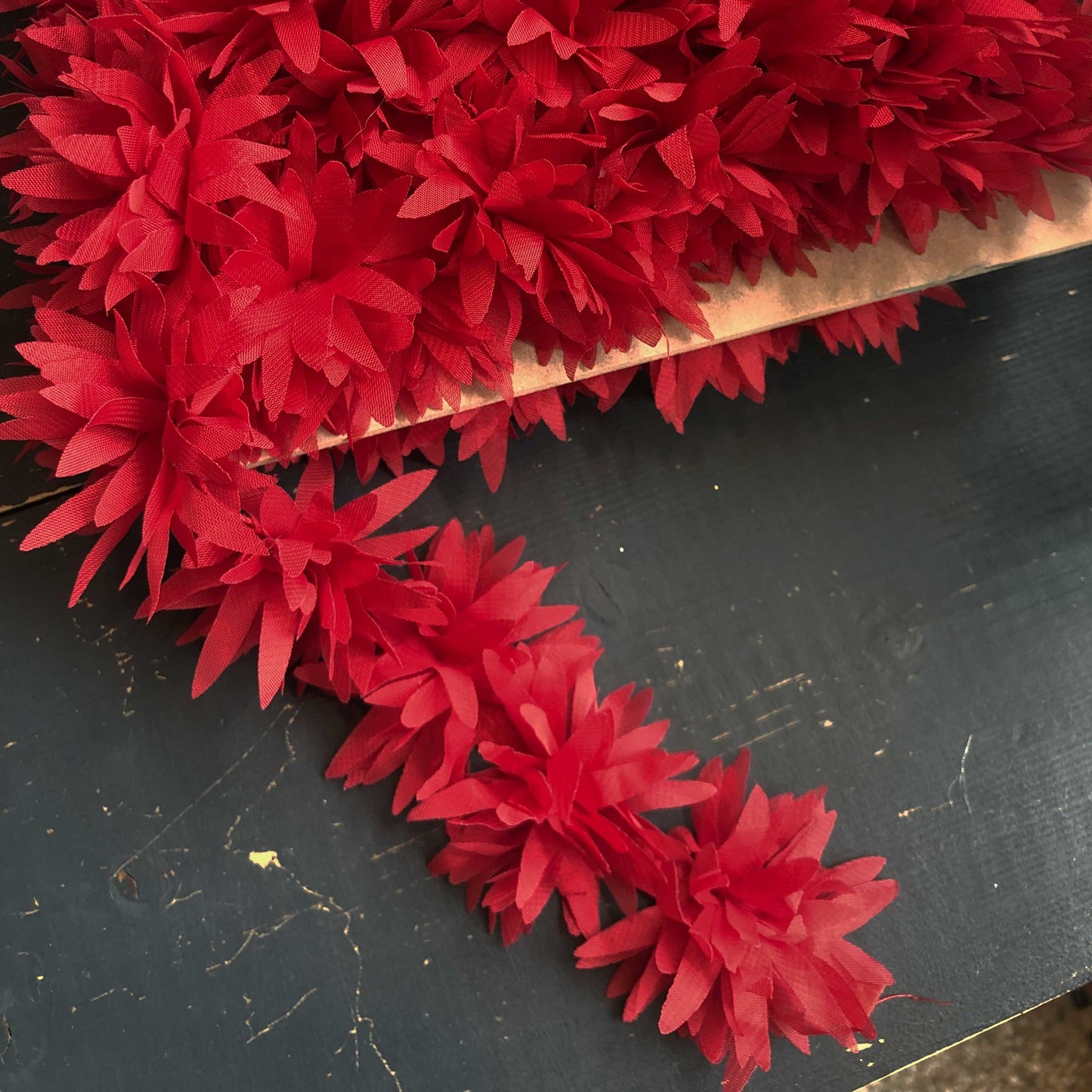 Dit speelse sierband is versierd met zachte, luchtige bloemetjes in een felrode tint. De bloemen zijn gemaakt van een lichte, doorschijnende stof die subtiel meebeweegt