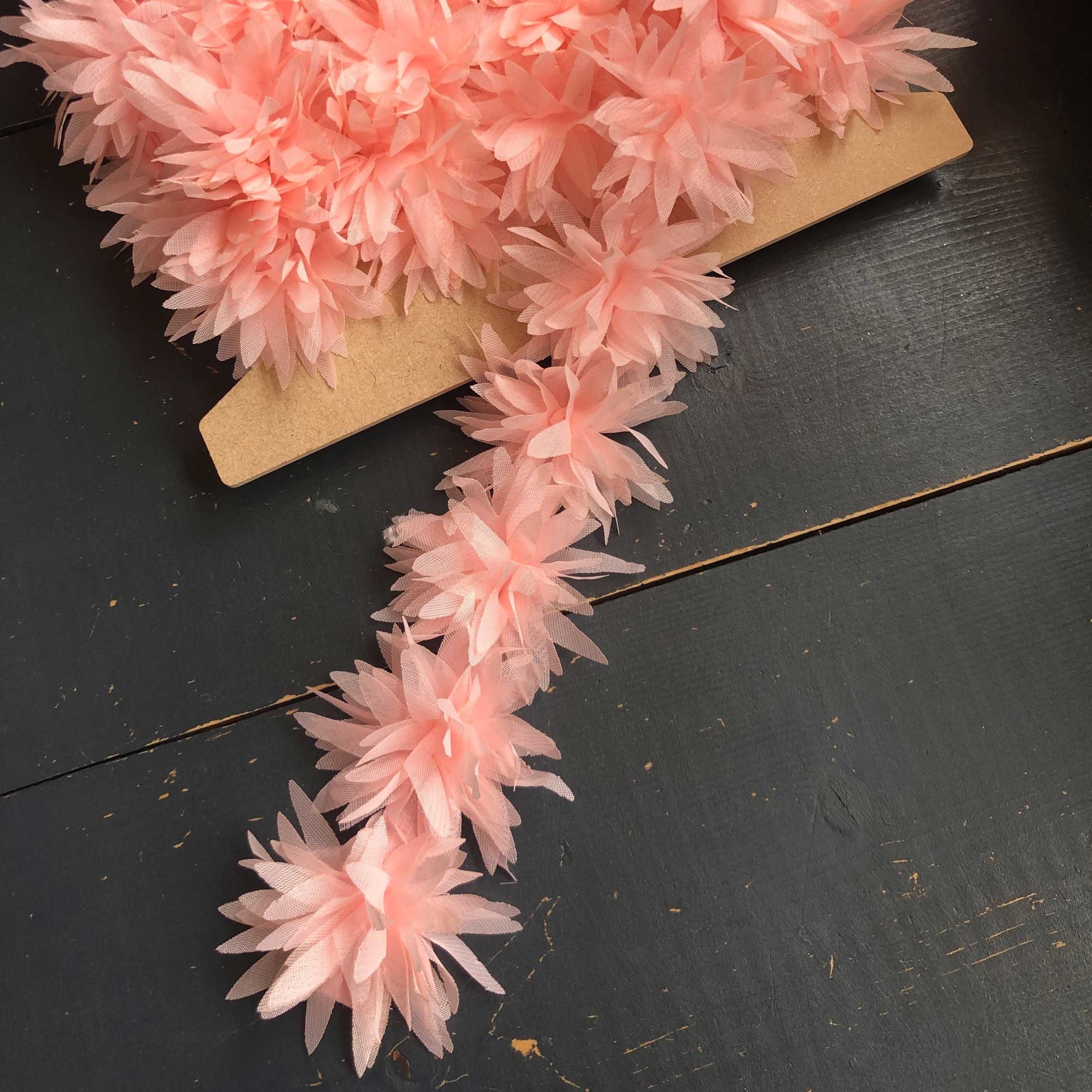 Dit speelse sierband is versierd met zachte, luchtige bloemetjes in een romantische zalmroze tint. De bloemen zijn gemaakt van een lichte, doorschijnende stof die subtiel meebeweegt