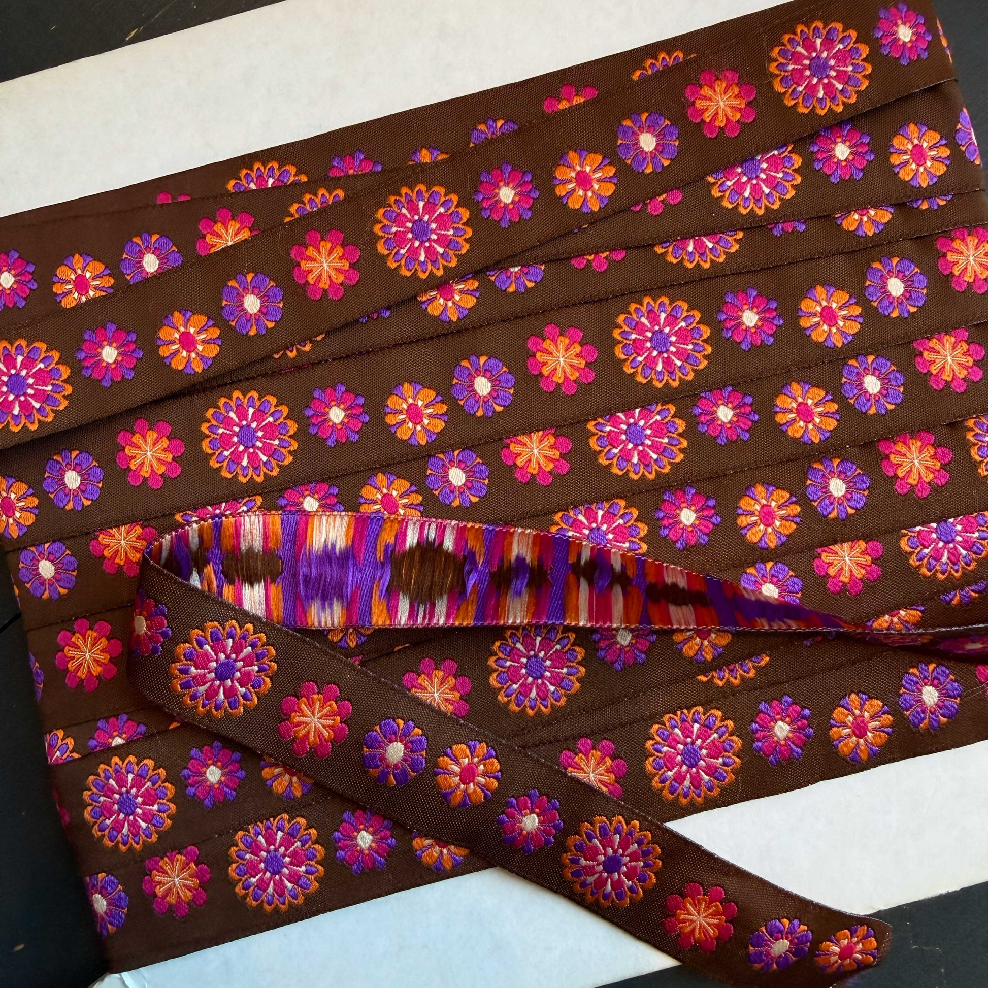 Dit sierband brengt je terug naar goede tijden! Prachtig sierband in een bruine kleur met vrolijke bloemen in oranje, roze en paarse kleuren.