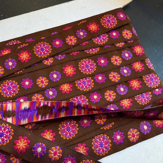 Dit sierband brengt je terug naar goede tijden! Prachtig sierband in een bruine kleur met vrolijke bloemen in oranje, roze en paarse kleuren.