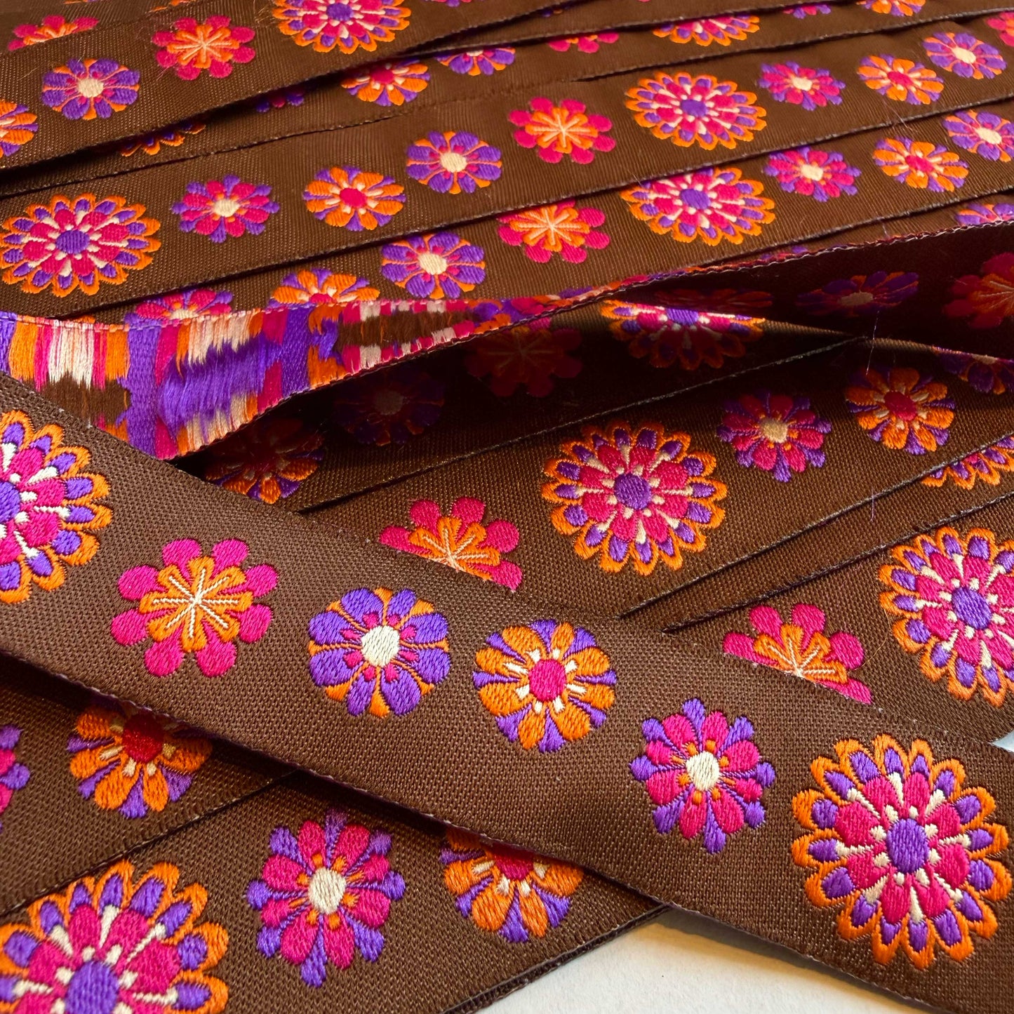 Dit sierband brengt je terug naar goede tijden! Prachtig sierband in een bruine kleur met vrolijke bloemen in oranje, roze en paarse kleuren.