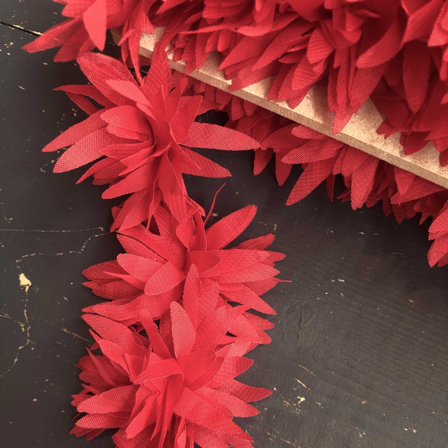 Dit speelse sierband is versierd met zachte, luchtige bloemetjes in een felrode tint. De bloemen zijn gemaakt van een lichte, doorschijnende stof die subtiel meebeweegt